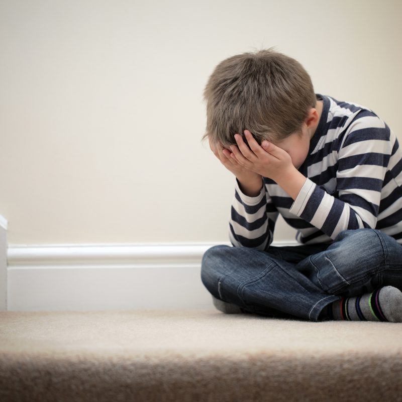 young child sitting down on stairs with head in hands, ofsted reports children's homes